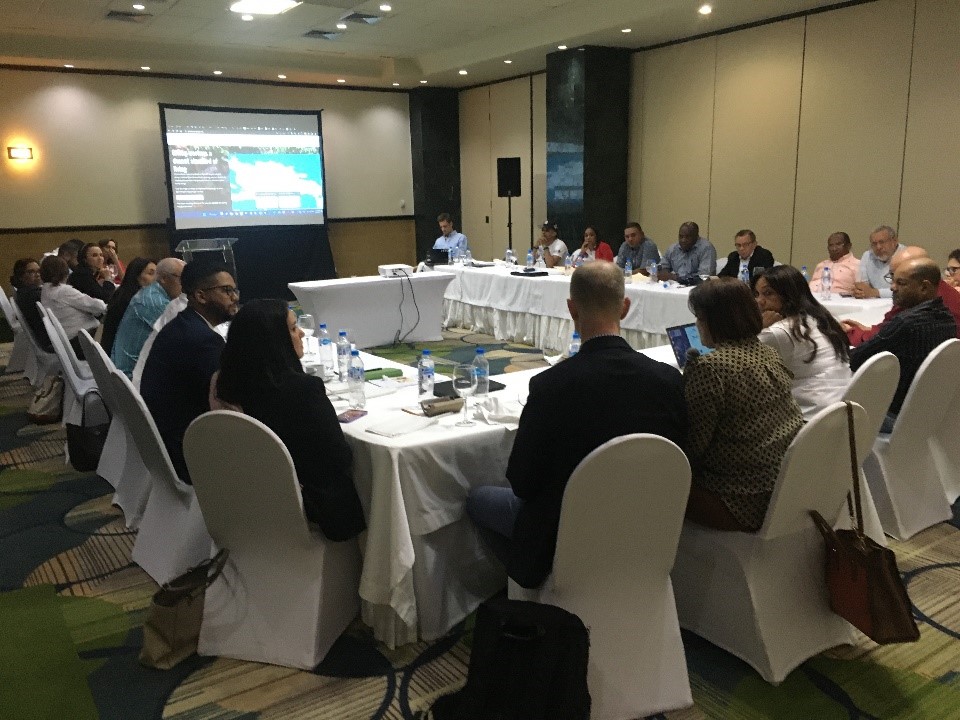 Photo of people around a u-shaped table in a conference room viewing a presentation